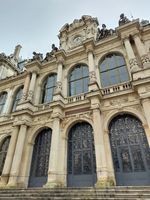 (2026) Façade du Palais de la Bourse du côté de la place de la Bourse. On peut voir l’horloge et les statues sur le toit. « Palais du Commerce » est inscrit en doré au-dessus de la porte principale.